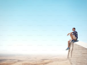 Jeune homme assis au sommet de la falaise et regardant le désert