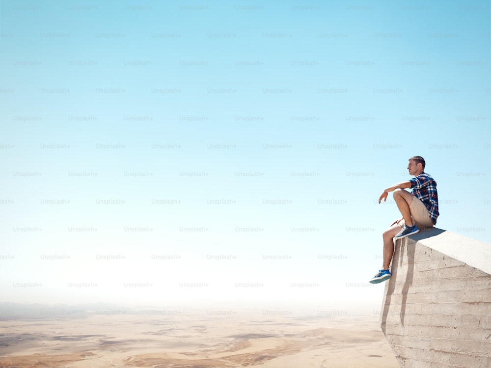 Junger Mann sitzt auf einer Spitze der Klippe und schaut auf die Wüste