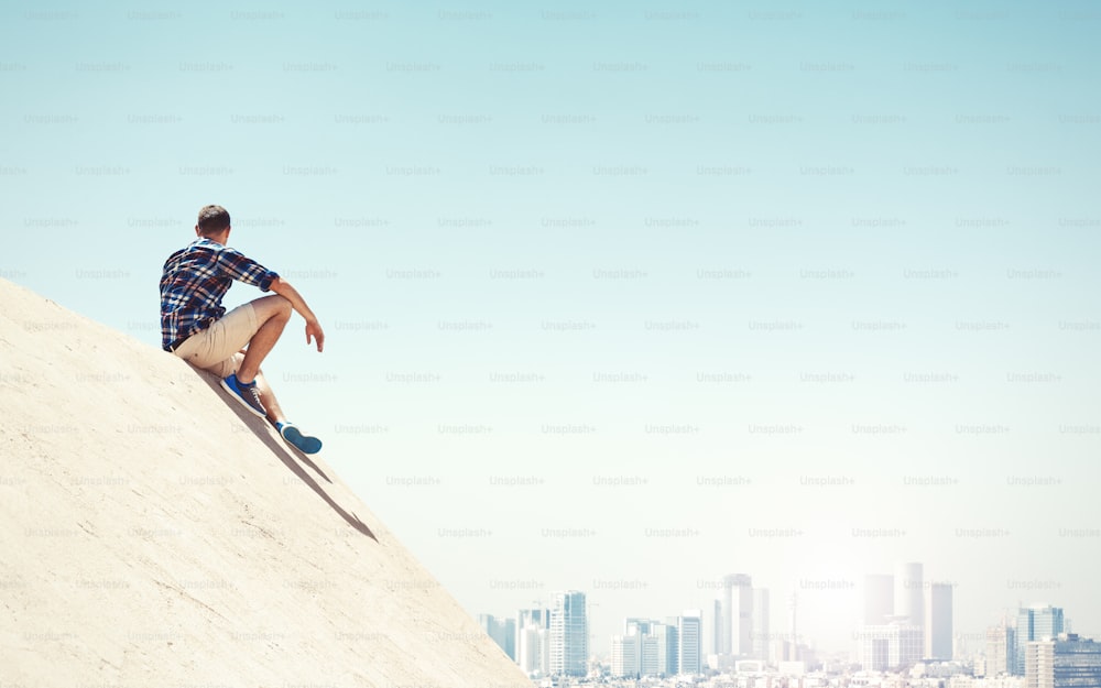 Young and risky man sitting on a peak and looking at the city