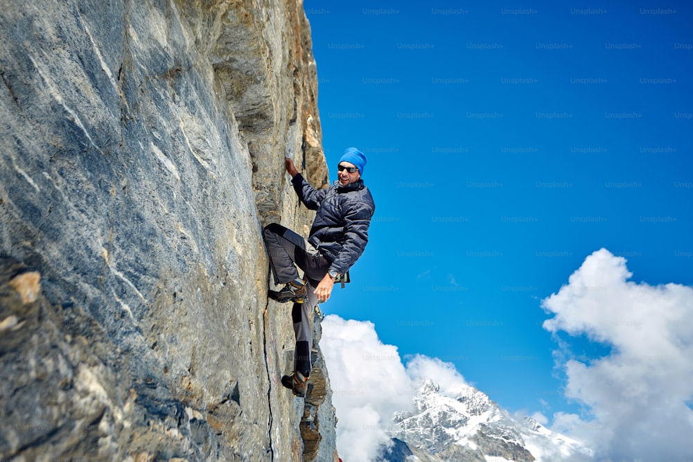 Junger Mann klettert auf eine Felswand, vor blauem Himmel