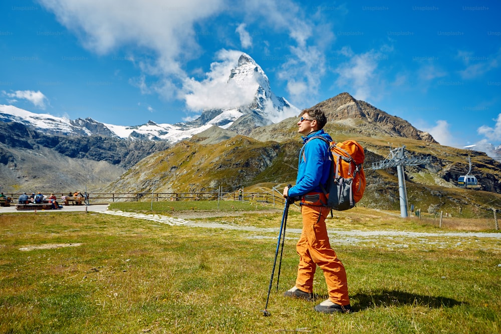 Wanderer mit Rucksack riecht einen Blumenkrokus auf dem Weg in den Aplser Bergen. Wanderung in der Nähe des Matterhorns