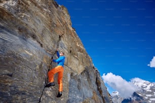Young man climbs on a rocky wall, against a blue sky