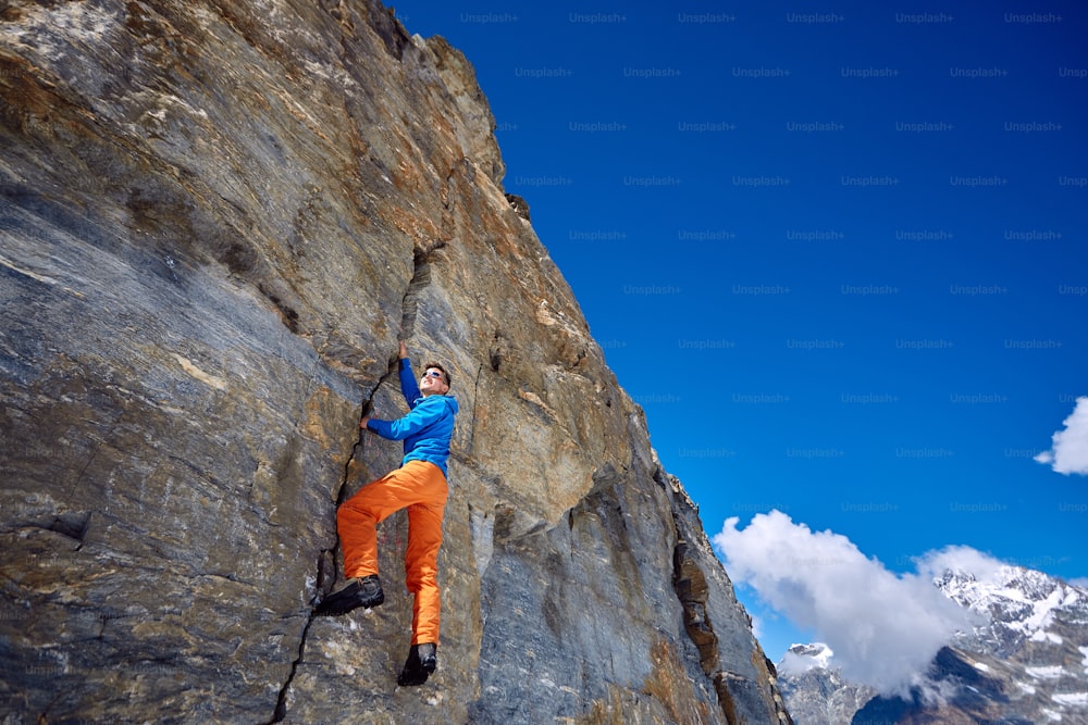 Young man climbs on a rocky wall, against a blue sky