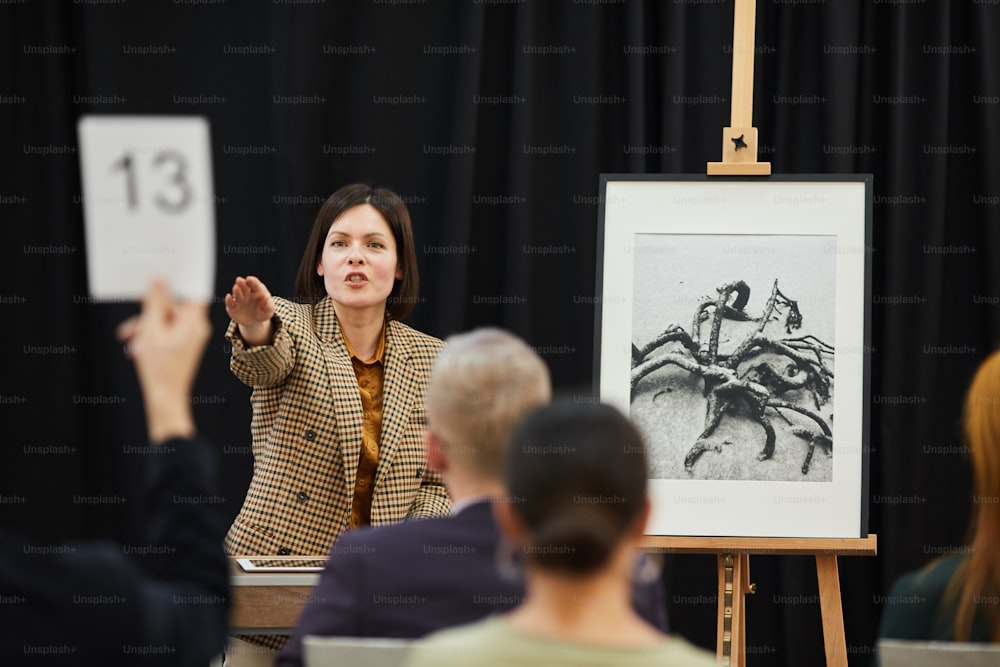 Businesswoman pointing at woman with sign and selling her the painting during auction