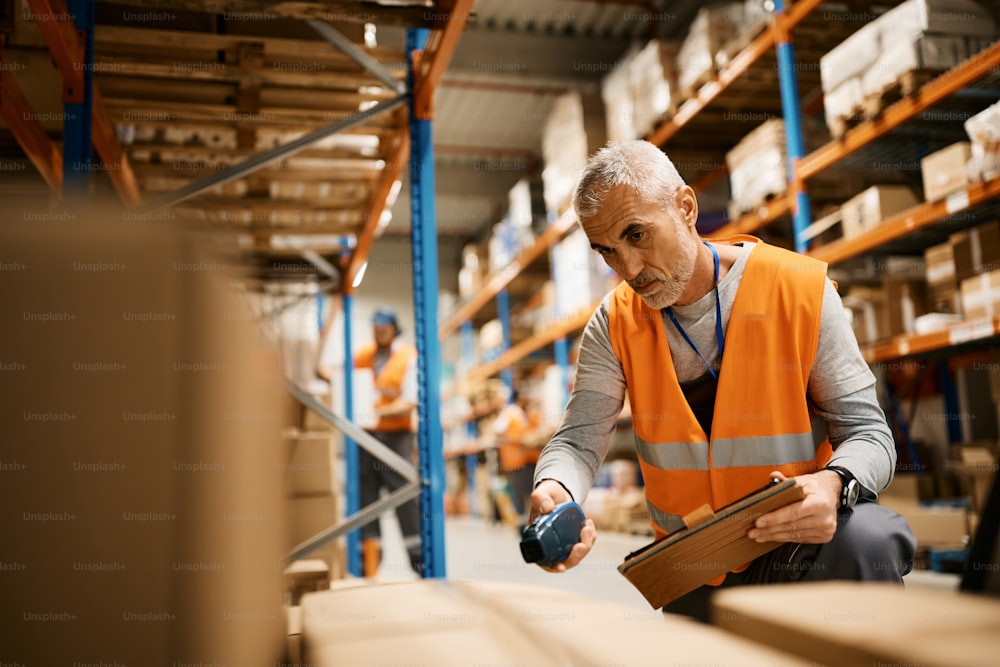 Mature worker using digital tablet and scanning labels on boxes while working in warehouse.