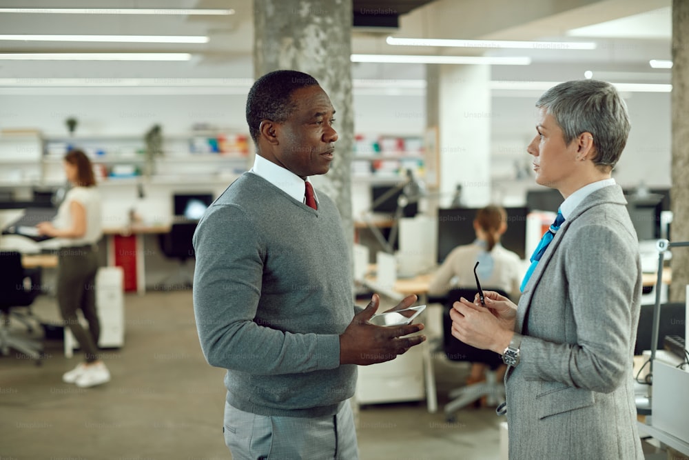 アフリカ系アメリカ人のビジネスマンがタッチパッドを使いながら、オフィスで同僚の女性とコミュニケーションをとっている。