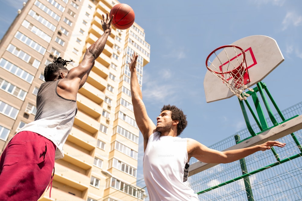 Zwei junge professionelle interkulturelle Basketballspieler in Activewear versuchen, den Ball zu fangen