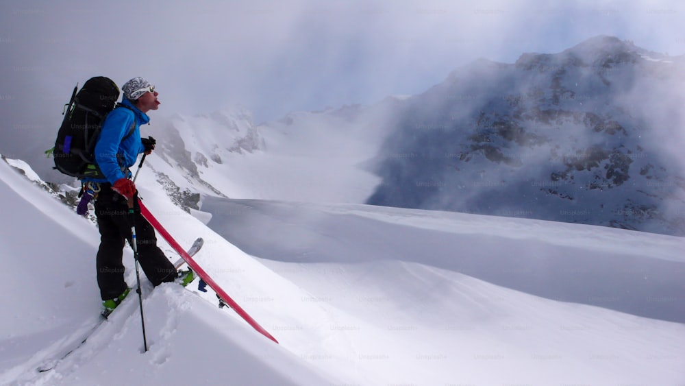높은 알프스 봉우리로 올라가는 남자 오지 스키어는 스위스 알프스의 아름다운 겨울날 가벼운 눈이 내리는 동안 놀고 어리석게 굴고 있습니다.