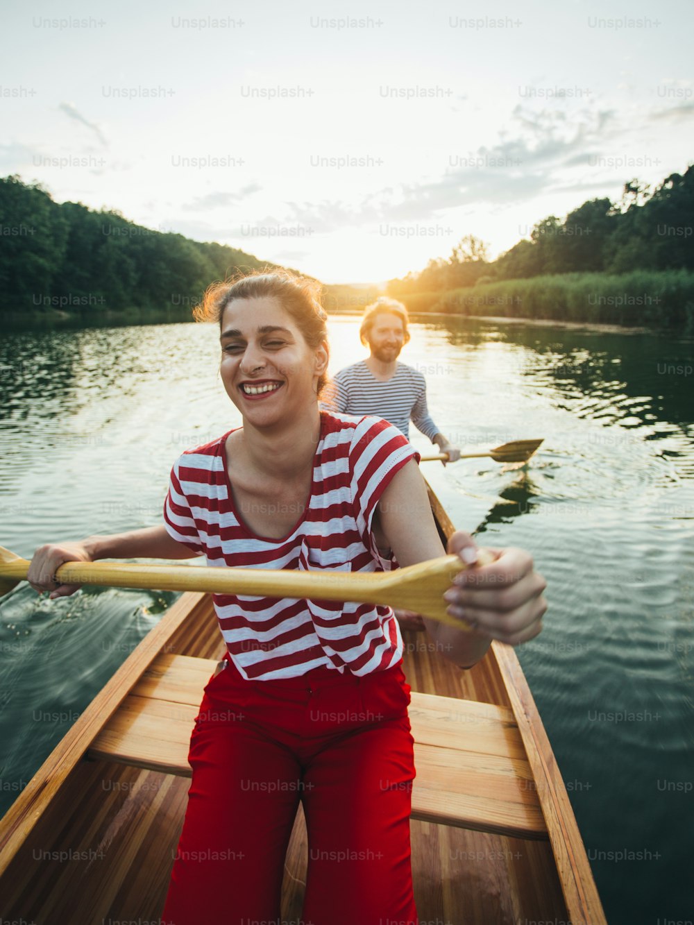Young woman paddling canoe with boyfriend on sunset lake.