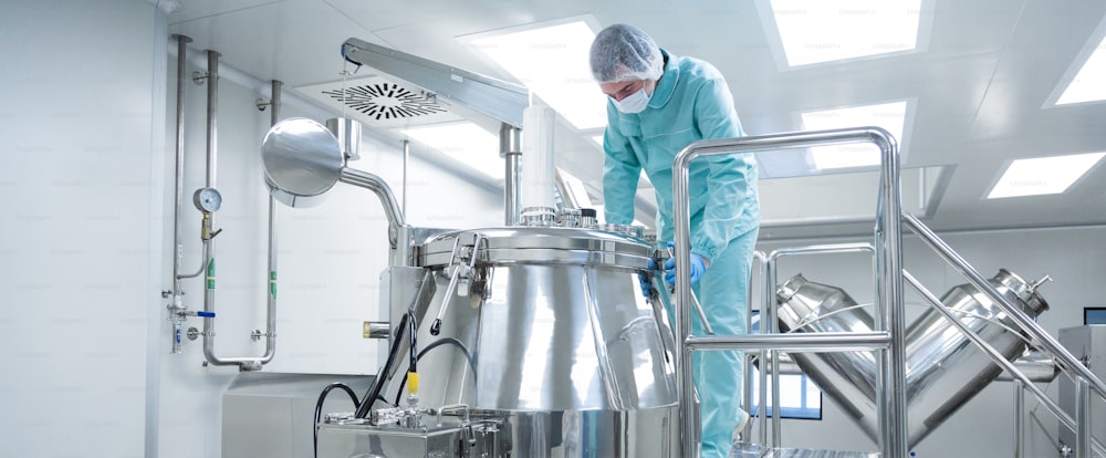 Pharmazeutische Fabrikarbeiterin in Schutzkleidung betreibt Produktionslinie in steriler Umgebung