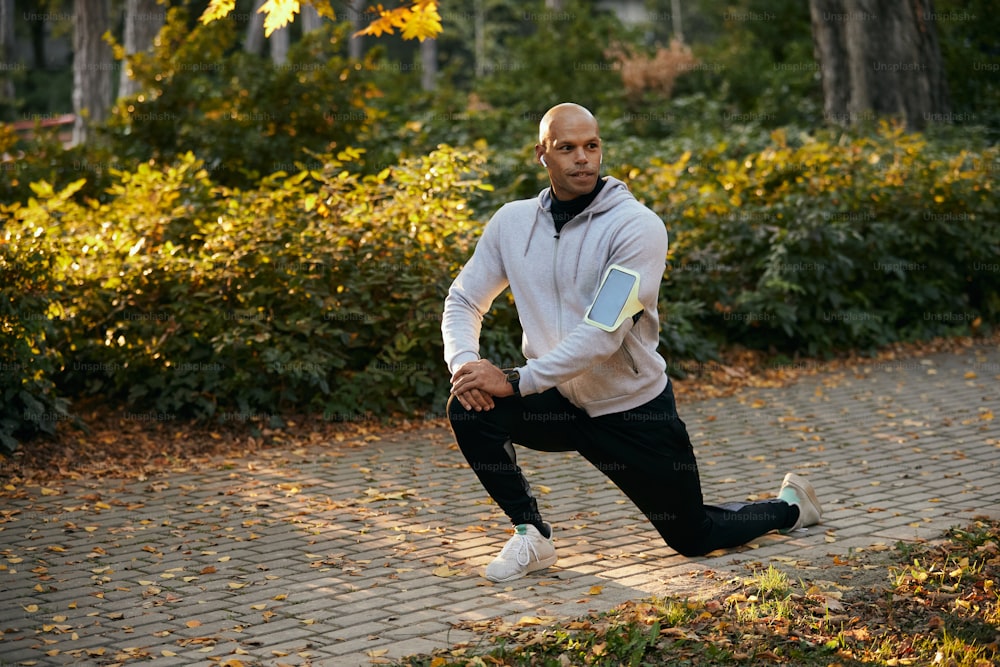Young black athlete warming up while having sports training in the park in autumn. Copy space.