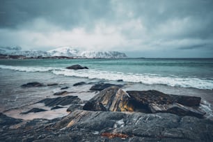 Ondas do mar norueguês na praia rochosa do fiorde. Praia de Ramberg, Ilhas Lofoten, Noruega