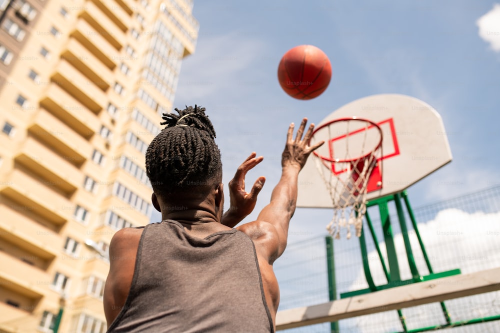 Rückansicht eines jungen afrikanischen Basketballspielers, der beim Training in städtischer Umgebung einen Ball in einen Korb wirft