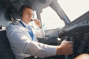 Male pilot in command controlling airplane while adjusting headset microphone closer to his mouth