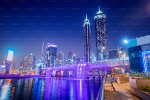 Illuminated waterfall bridge in downtown Dubai at night with thousands of small lights on high skyscrapers. Popular tourist attractions in UAE