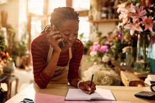 若いアフリカ系アメリカ人の花屋は、花屋で注文を受けながら携帯電話で話し、メモを取ります。