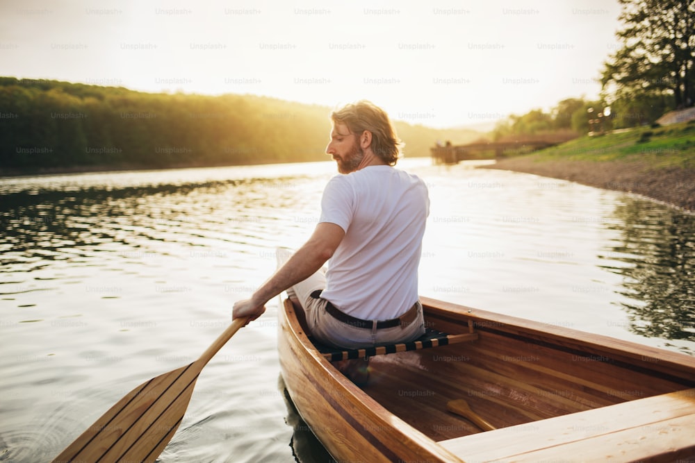 Vista posteriore del canoista maschio che rema sulla canoa di legno con il remo.