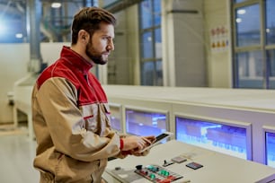Ouvrier utilisant un pavé tactile tout en supervisant une machine de ligne de production automatisée dans une usine de menuiserie.