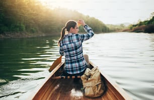 Rear view of hipster girl paddling the canoe on the sunset lake.