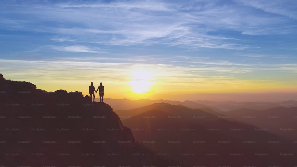 Las dos personas de pie en la montaña en el hermoso fondo de la puesta de sol