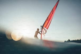 ウィンドサーフィンボードでバランスをとるサーファーのシルエットをローアングルで見る。