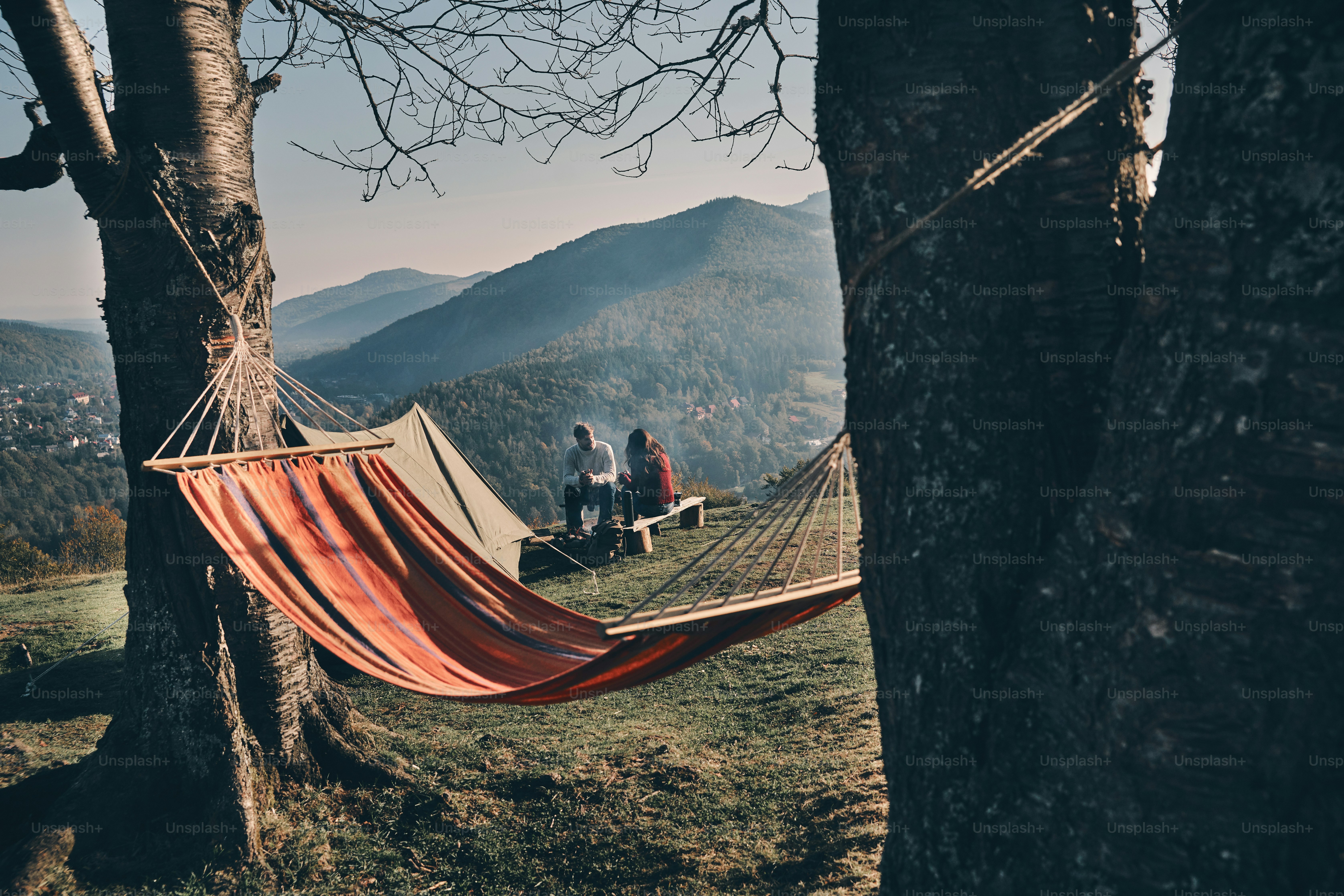 Young couple having breakfast while sitting by the campfire in mountains
