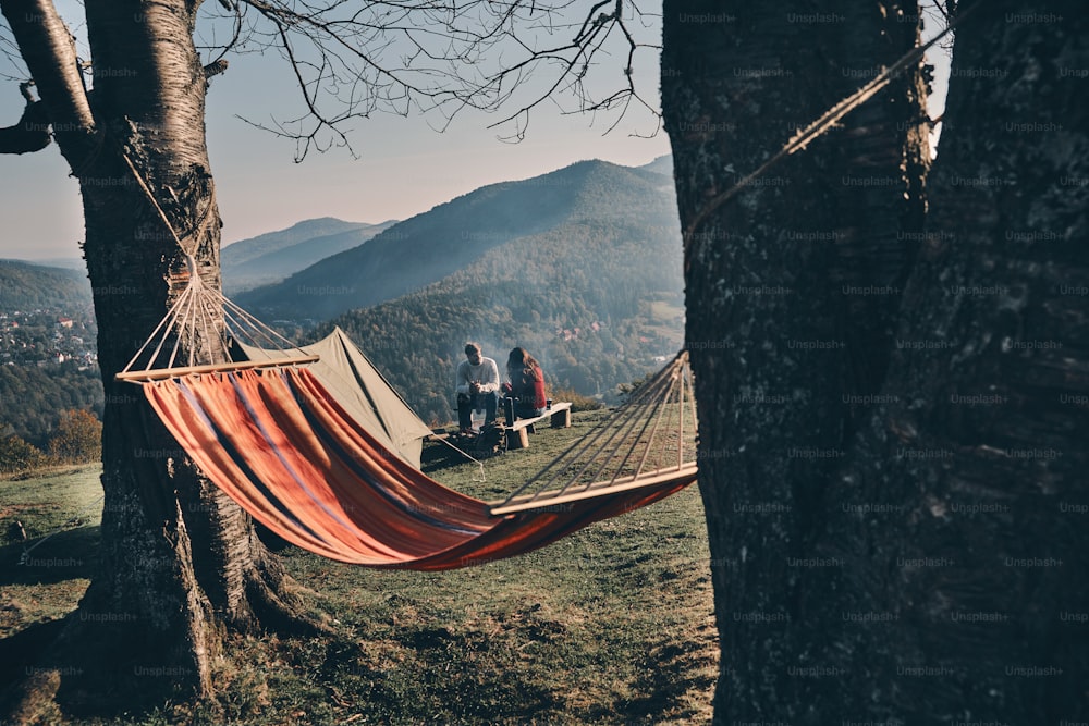 Jovem casal tomando café da manhã enquanto está sentado à beira da fogueira nas montanhas