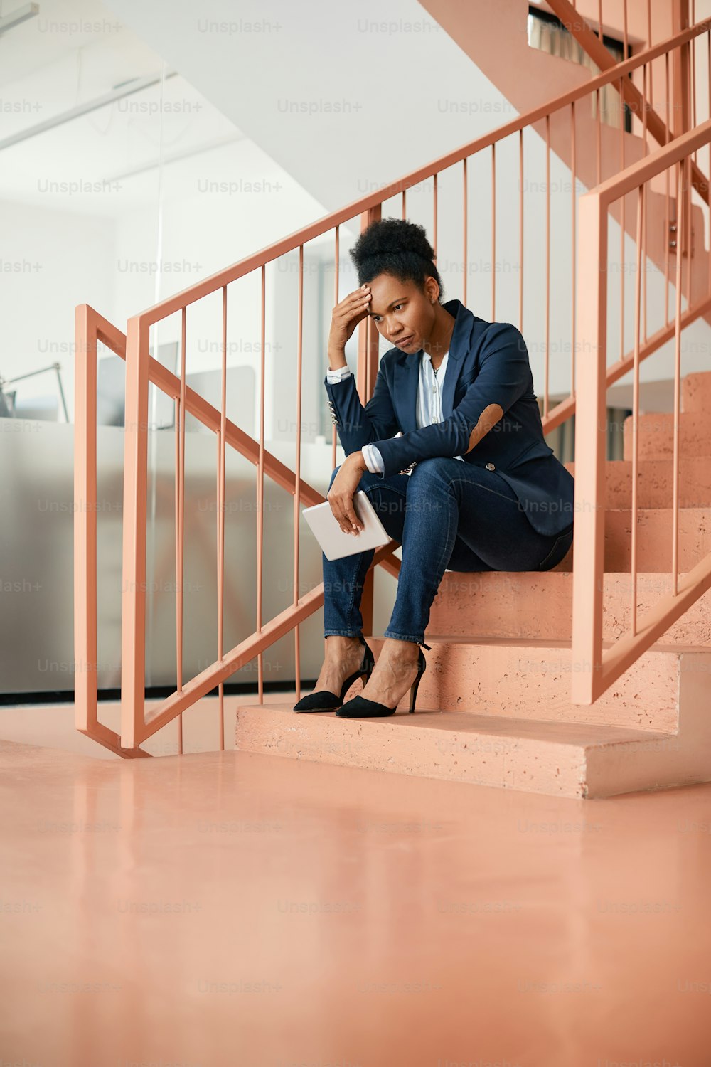 Distraught African American businesswoman thinking of something while sitting on a staircase in hallway. Copy space.