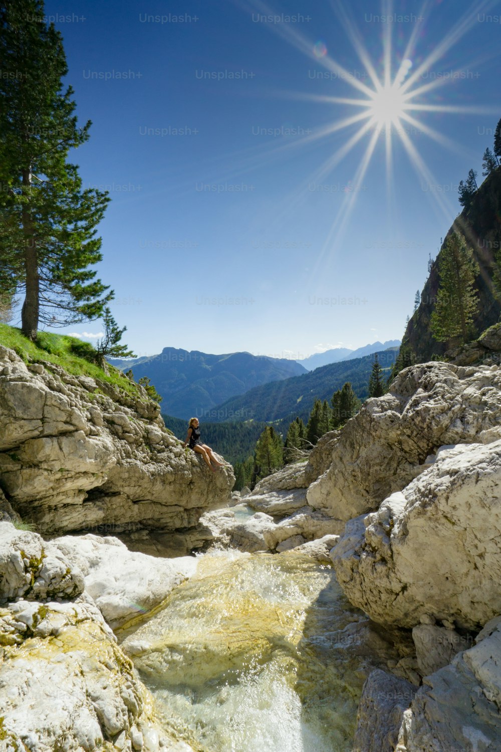 young attractive woman relaxing on a rock on the side of a small mountain stream in a picturesque mountain landscape in the Dolomites of Italy