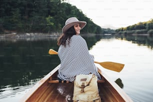 Joven sonriente remando en la canoa en el lago al atardecer.