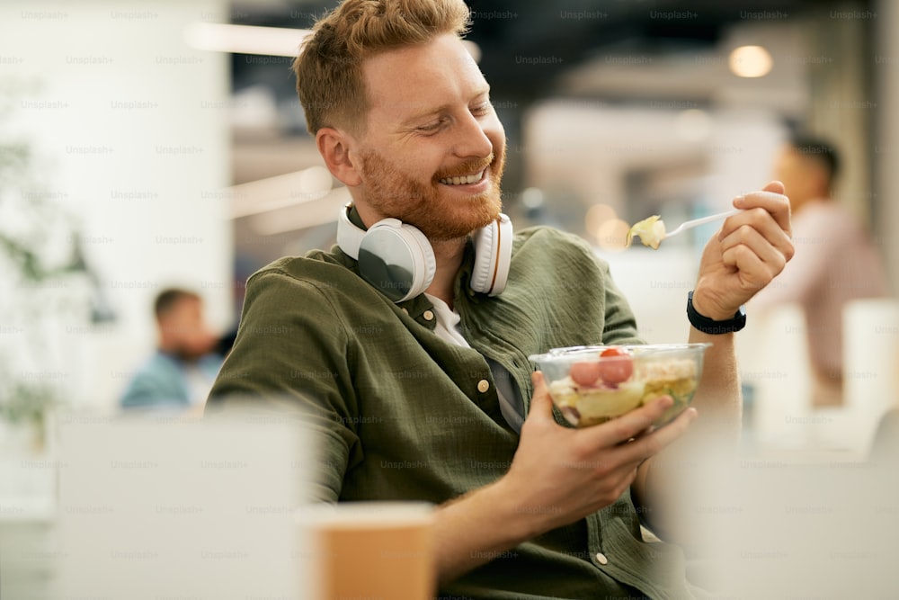 Hombre de negocios feliz que tiene una comida saludable durante la pausa del almuerzo en el trabajo.