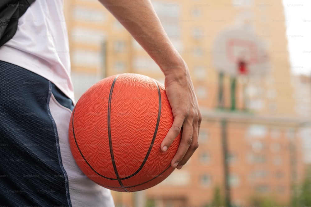 Main d’un jeune joueur de basket-ball professionnel tenant le ballon tout en allant s’entraîner sur le terrain de jeu