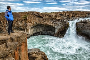 Reisende wandern in der isländischen Sommerlandschaft am Aldeyjarfoss Wasserfall in Nordisland. Der Wasserfall befindet sich im nördlichen Teil der Sprengisandur Road im isländischen Hochland.