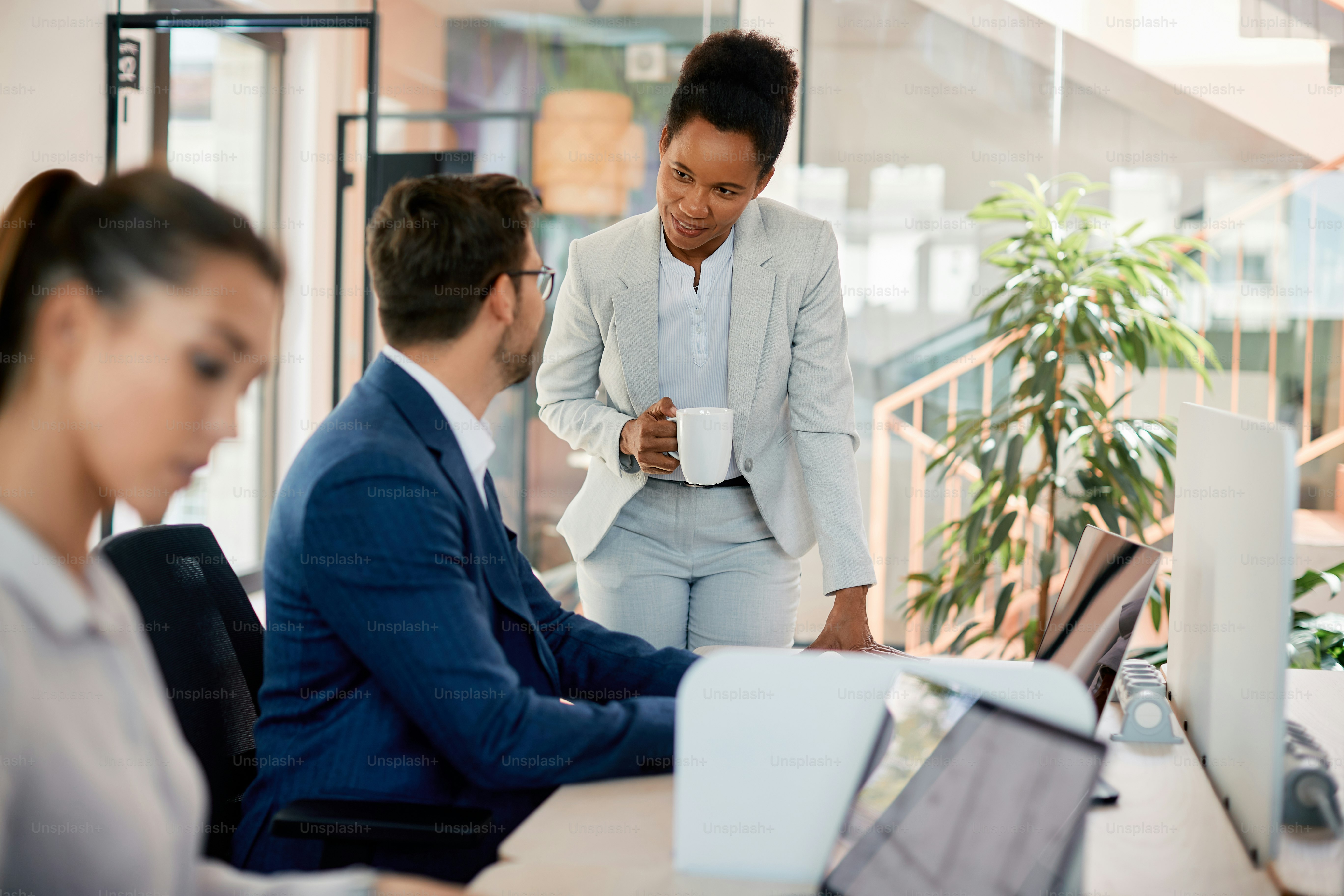 Happy African American businesswoman communicating with male coworker while he is working on a computer in the office.