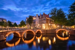 夕暮れ時の運河、橋、中世の家々がライトアップされたアムステルダムの街並みの夜景。アムステルダム、オランダ