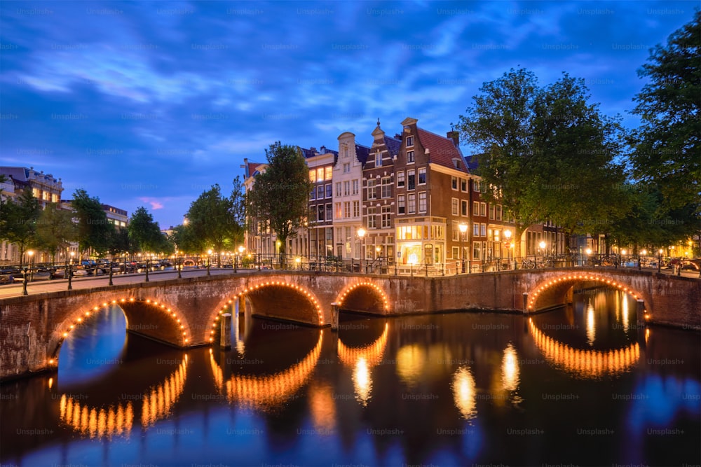 Vue nocturne du paysage urbain d’Amterdam avec canal, pont et maisons médiévales au crépuscule du soir illuminé. Amsterdam, Pays-Bas