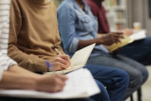 Close-up of group of people sitting on chairs and making notes in notebooks during seminar