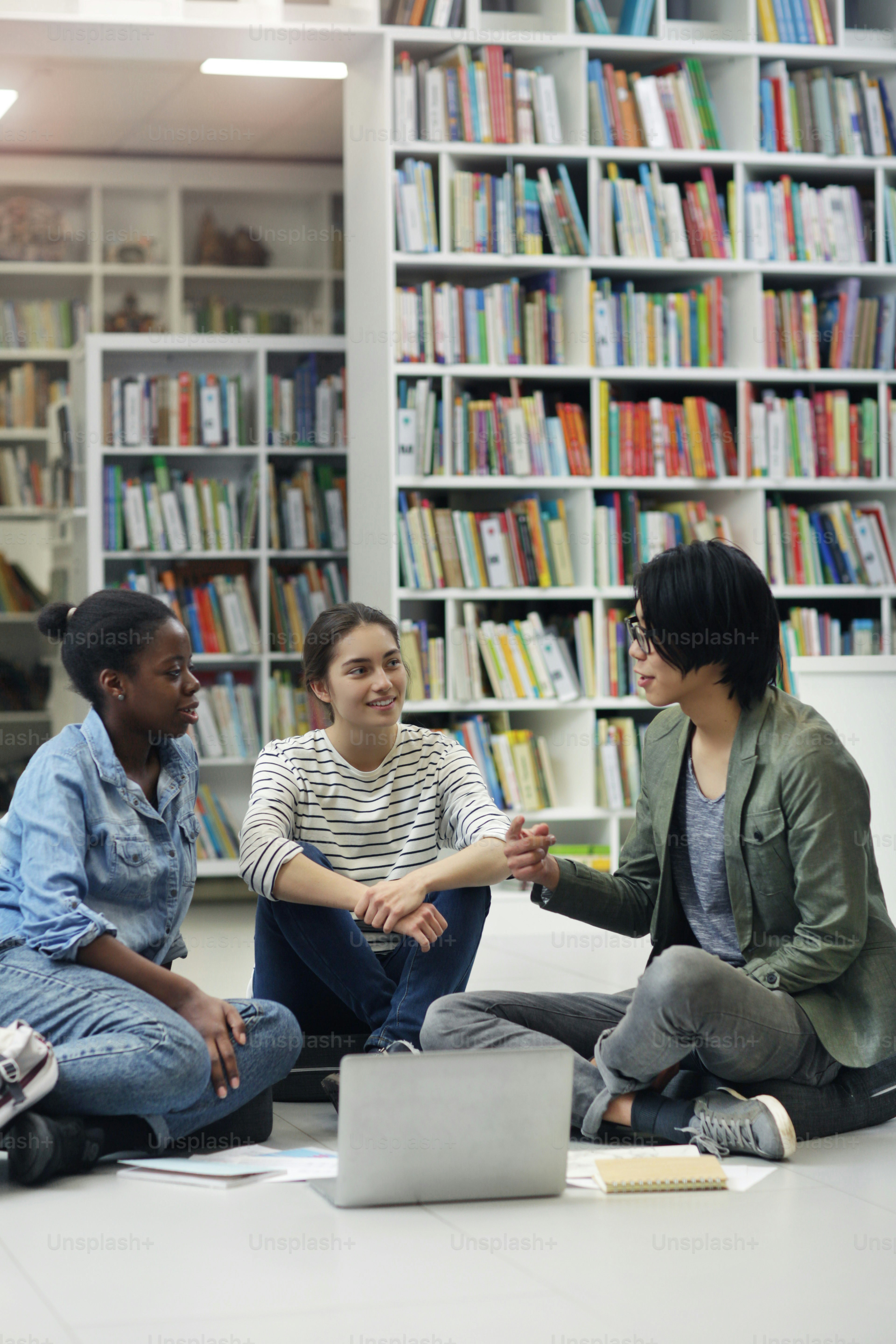 Group of students sitting on the floor with laptop and listening to their friend who explaining the task they are in the library