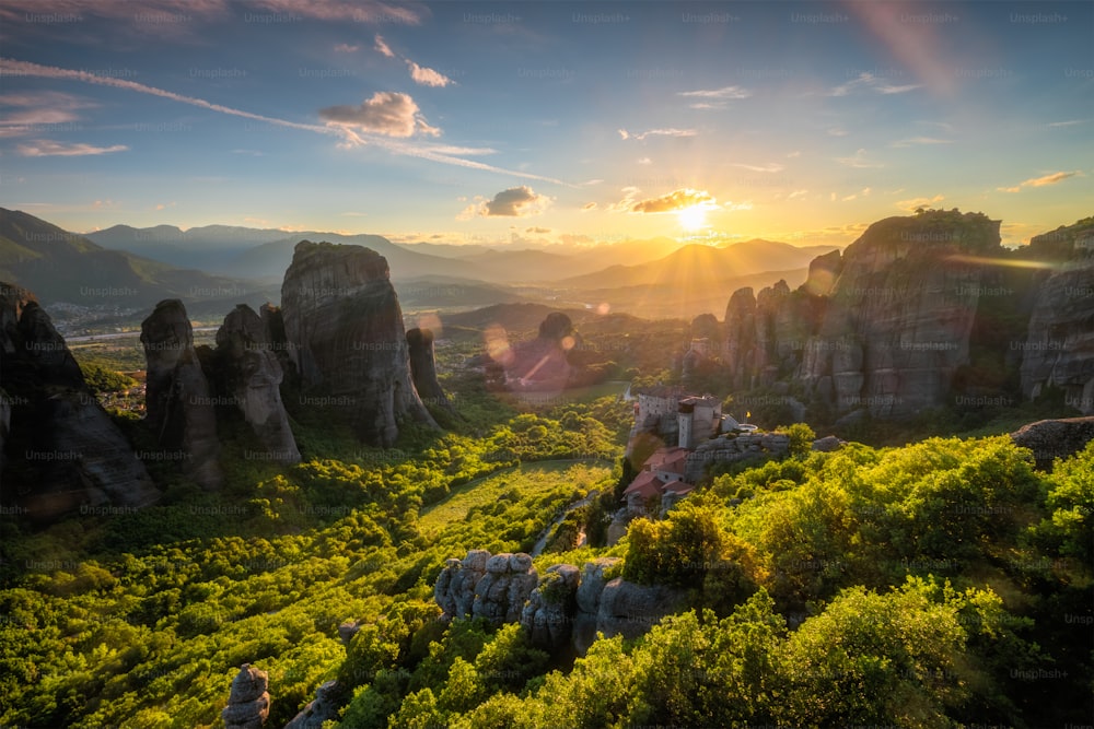Pôr do sol sobre o mosteiro de Rousanou e o Mosteiro de São Nicolau Anapavsa no famoso destino turístico grego Meteora, na Grécia, ao pôr do sol com raios de sol e reflexo de lente