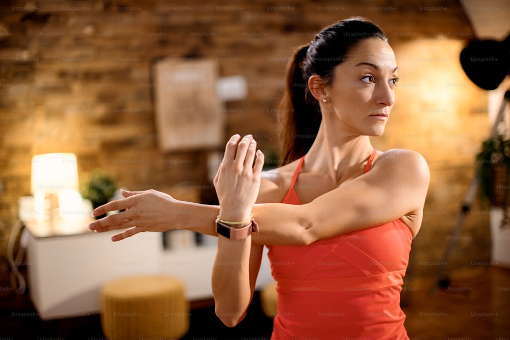 Athletic woman working out at home and stretching her arm while warming up.