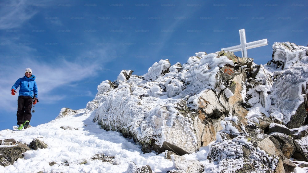 männlicher Skitourengeher am Gipfelkreuz eines hochalpinen Gipfels an einem schönen Wintertag in den Schweizer Alpen