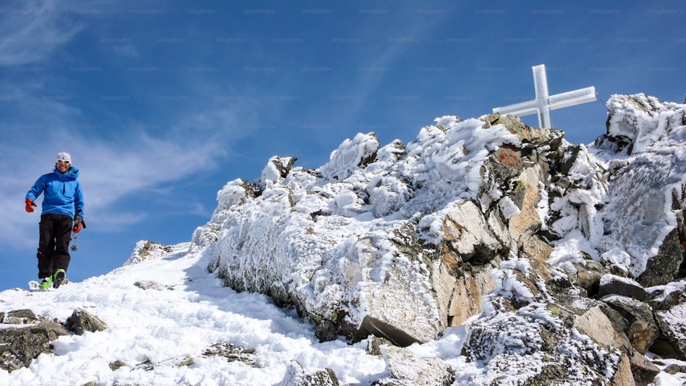 male backcountry skier at the summit cross of a high alpine peak on a beautiful winter day in the Swiss Alps