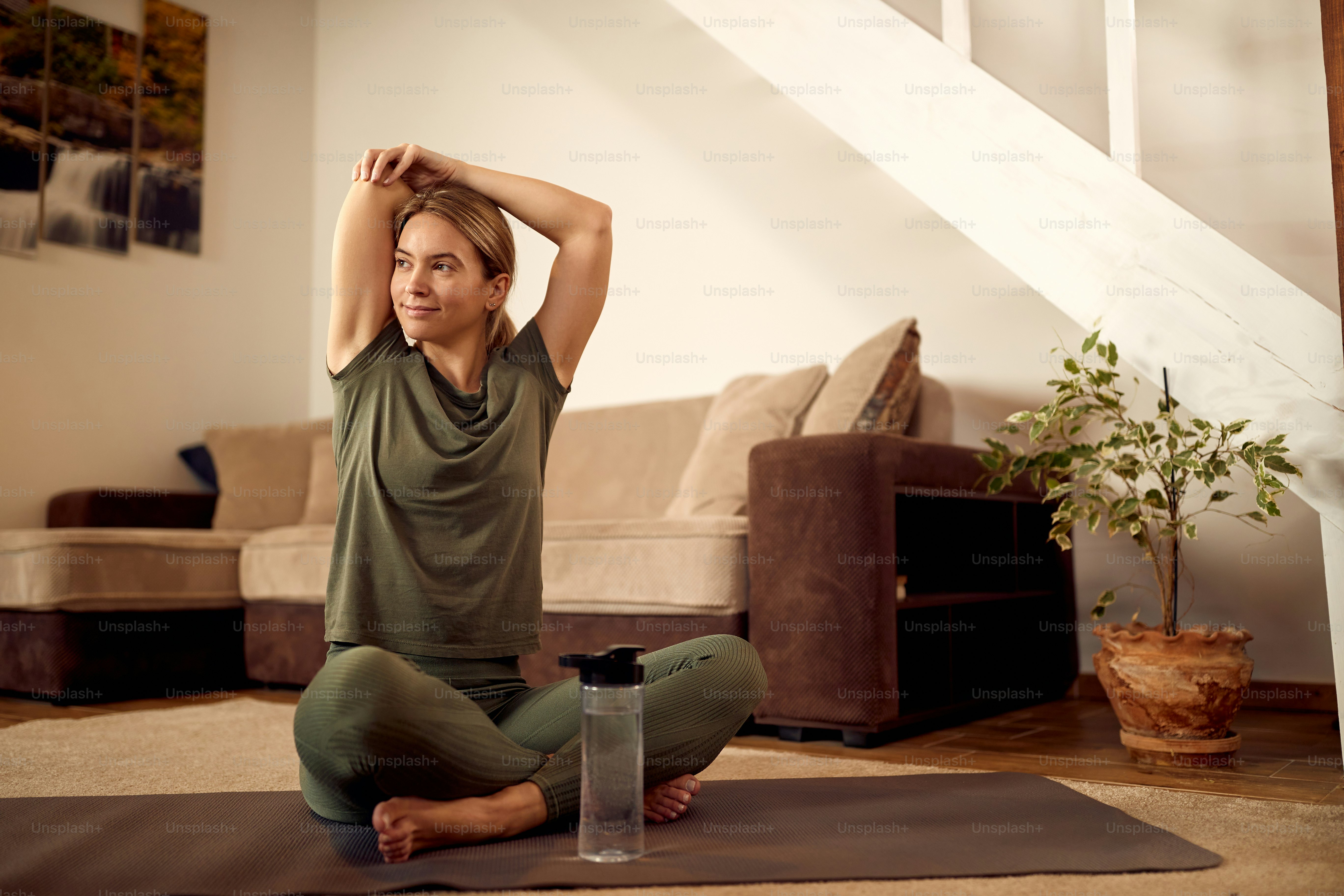 Smiling athletic woman doing stretching exercises while waring up for sports training at home.
