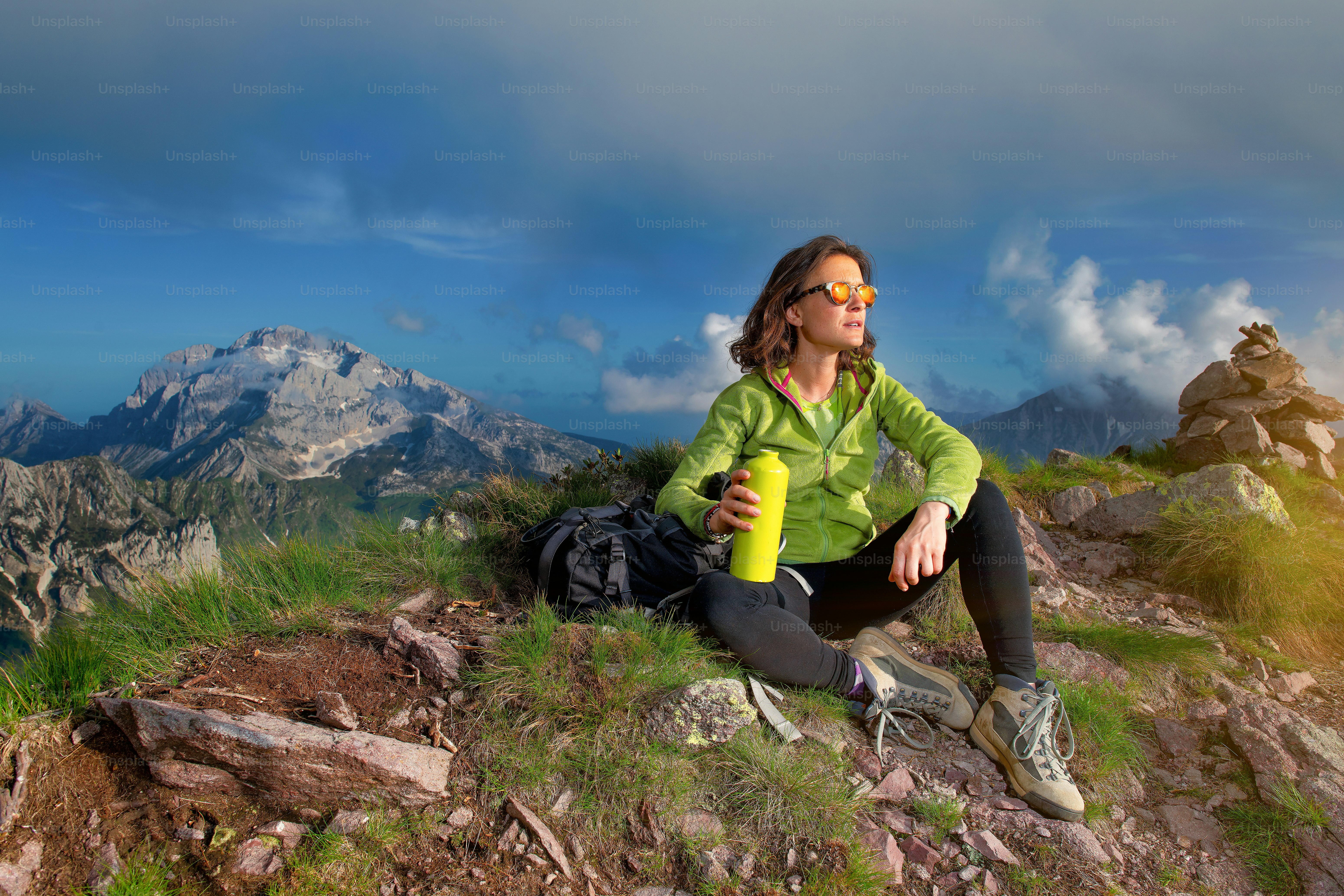 A girl rests after climbing the top of a mountain. He drinks from his borrazzia and observes the sunset