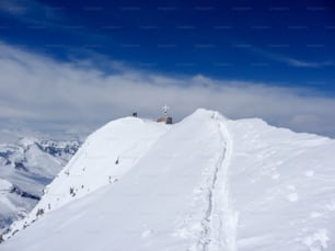 Skitourengeher und Bergsteiger in der Nähe eines hochalpinen Gipfelkreuzes in den österreichischen Alpen mit einem schmalen und exponierten Grat, der zu ihnen führt
