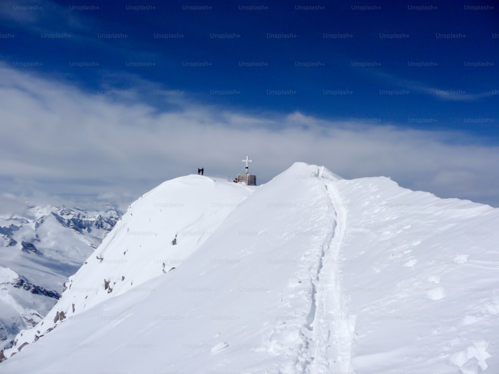 scialpinisti e alpinisti nei pressi di una croce di vetta in alta montagna nelle Alpi austriache con una cresta stretta ed esposta che porta verso di loro