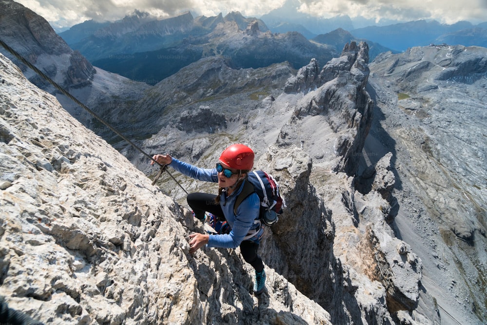 Jovem alpinista feminina em uma íngreme e exposta Via Ferrata nas Dolomitas italianas com uma vista fantástica dos arredores