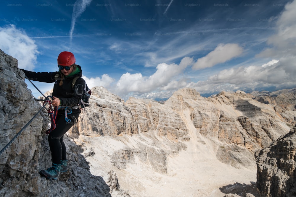 junge Kletterin auf einem Klettersteig in den Dolomiten mit traumhafter Berglandschaft im Rücken