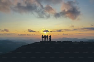 Las cuatro personas de pie en la hermosa montaña en el fondo de la puesta de sol