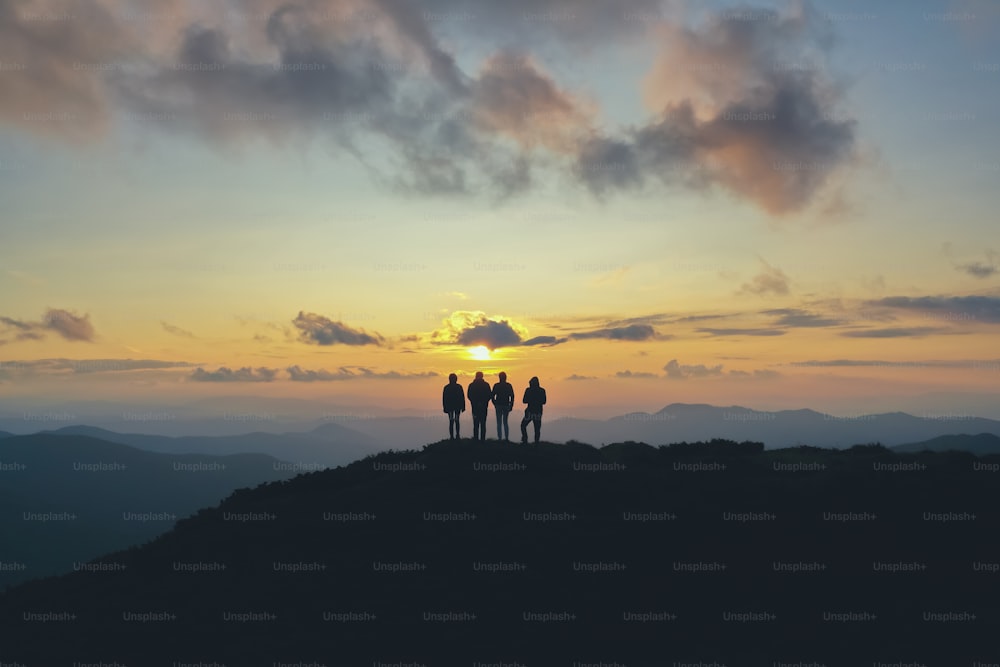 Las cuatro personas de pie en la hermosa montaña en el fondo de la puesta de sol
